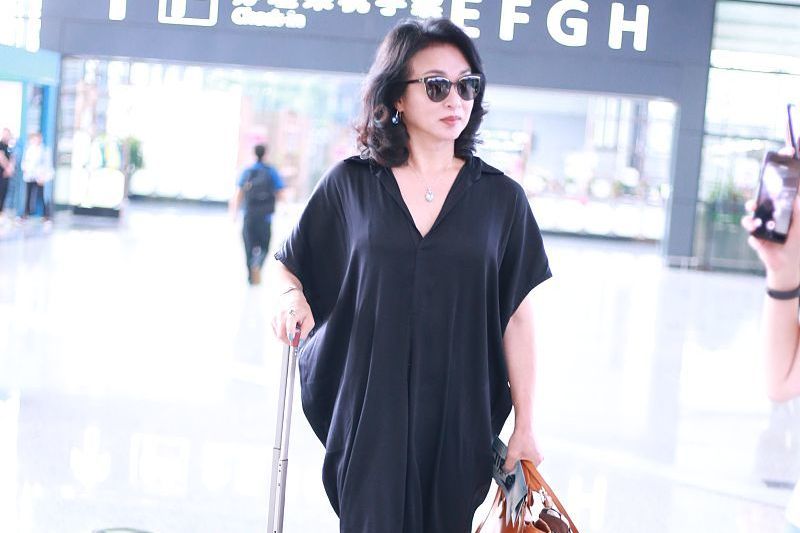52岁金星穿宽松长裙走机场，难掩魁梧身形，戴墨镜披散发气场强大